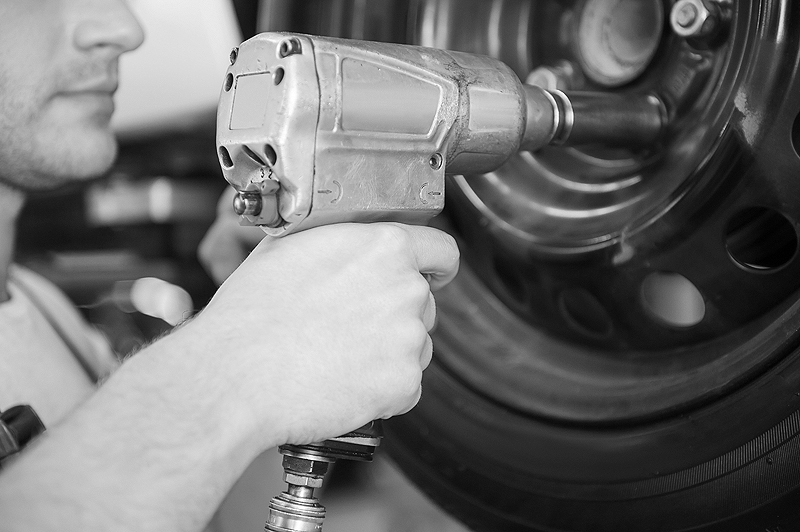 Removing tires from car. Close-up of young man using pneumatic wrench while working with car tire in workshop